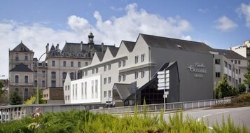 Un hotel con fachada moderna, una entrada destacada y un edificio tradicional en el fondo.