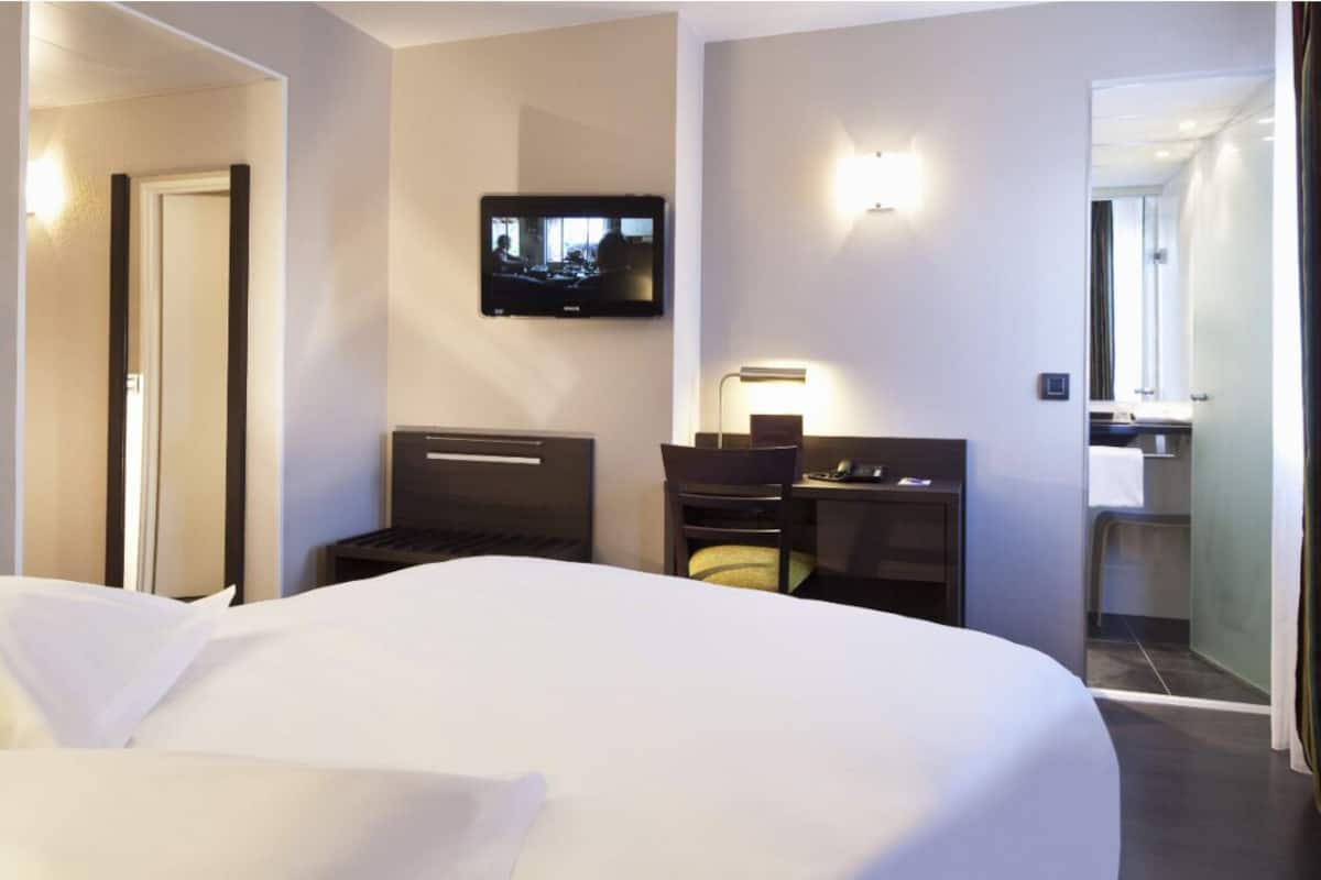 A hotel room with a large bed, a television mounted on the wall, a desk with a chair, and a mirror.
