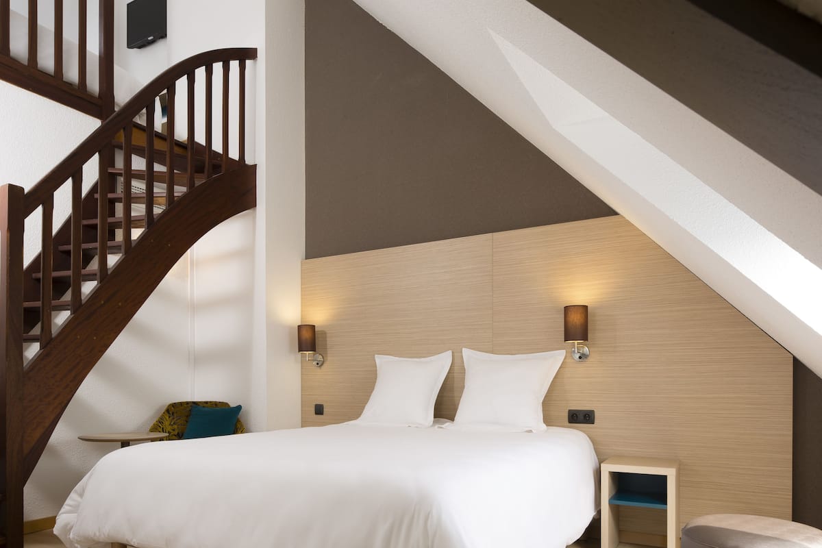 Een slaapkamer met een houten trap, een bed met witte lakens, twee wandlampen en een klein nachtkastje.