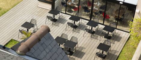 An outdoor patio with tables and chairs, a glass enclosure, and a metal pipe.