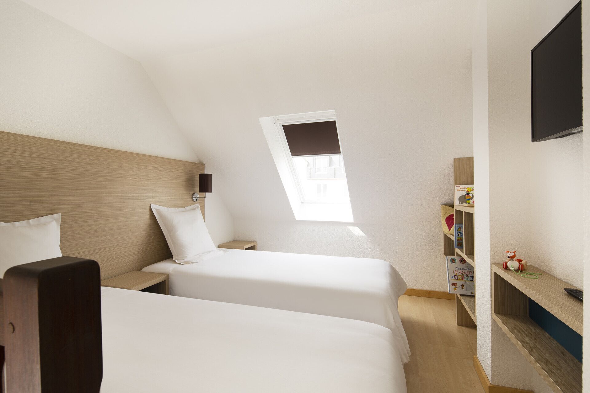 A bedroom with two beds, a small bedside table, a nightstand, a bookshelf, and a TV on the wall.
