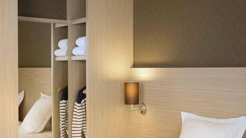 Une chambre d’hôtel avec un lit, une armoire où sont suspendus des vêtements et une lampe fixée au mur.