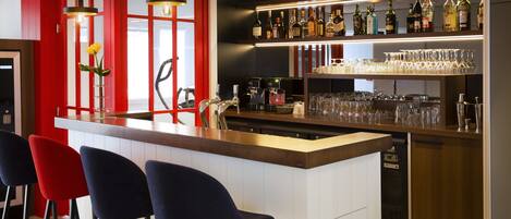 A bar area with a counter, stools, and shelves of bottles and glasses.