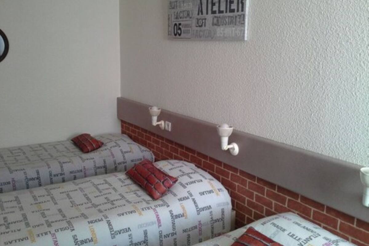 A room with two beds covered in patterned bedding, a brick accent wall, and a white shelf with two white lamps.