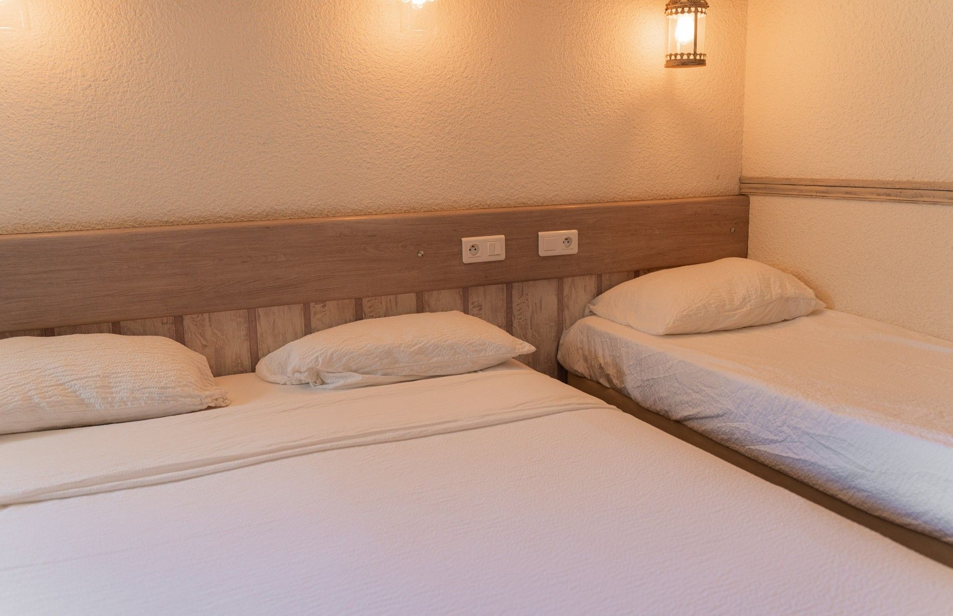 Una habitación de hotel con dos camas individuales, un cabecero de madera y dos lámparas fijadas a la pared.