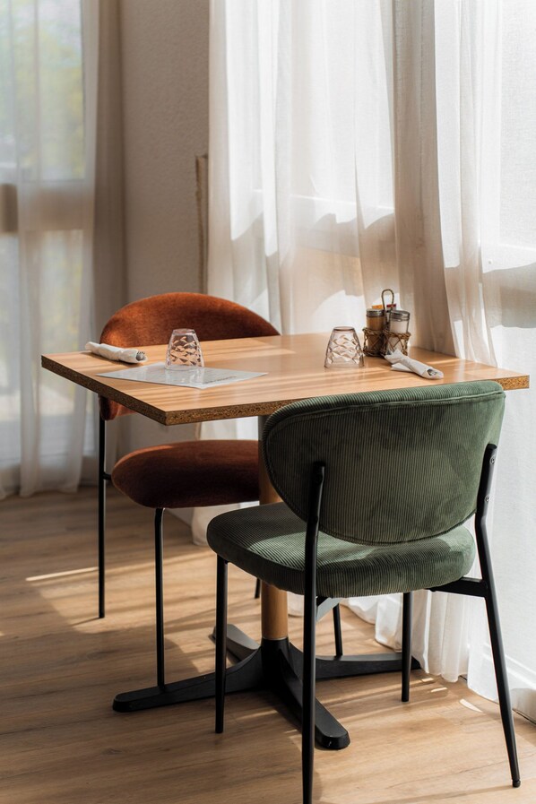 A dining area with a wooden table, two chairs, and a window with sheer curtains.