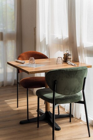 A dining area with a wooden table, two chairs, and a window with sheer curtains.
