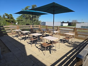 An outdoor patio with tables and chairs, umbrellas, and a wooden fence.