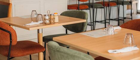 A restaurant interior with wooden tables and chairs, a kitchen area, and a clock on the wall.