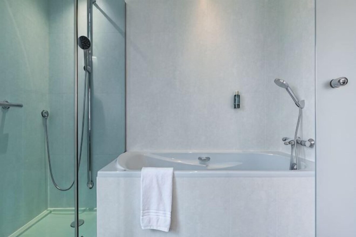 Un baño moderno con bañera, ducha y zona de ducha con mampara de vidrio.