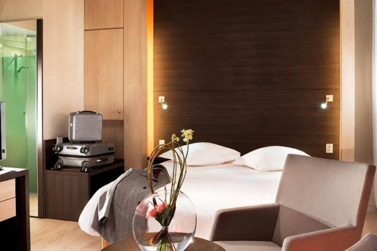 Una habitación de hotel moderna con una cama, un escritorio con ordenador y un jarrón con flores.