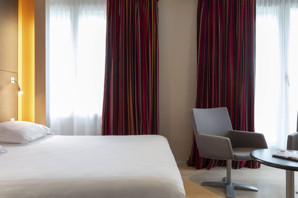 Una habitación de hotel con una cama, una silla, una mesita y cortinas.