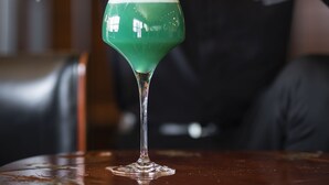 A person pouring a green cocktail into a martini glass with a lemon slice on the rim. - Oceania Brest Centre (Brest)