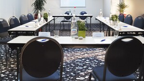 A conference room with a high ceiling, recessed lighting, and a large screen at the front. Tables are set with chairs, water bottles, and a potted plant. - Oceania Brest Centre (Brest)