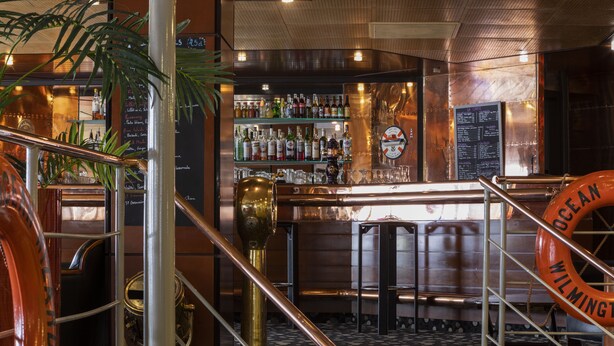 A bar area with a metal railing, a life preserver, and a variety of bottles on shelves. - Oceania Brest Centre (Brest)
