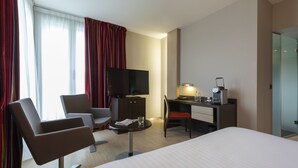 A hotel room with a bed, two armchairs, a desk with a computer, a TV, and a small table with a magazine and glass. - Oceania Brest Centre (Brest)