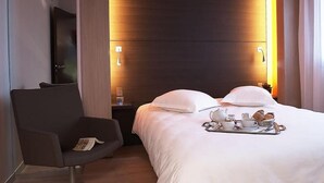 Habitación de hotel con cama, silla, mesita de noche y una bandeja con alimentos para el desayuno.