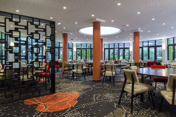 A spacious indoor dining area with multiple tables and chairs, large windows, and a decorative wall.
