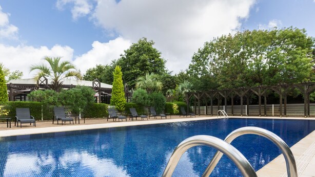 Una piscina con sillones de descanso y una pérgola al fondo.