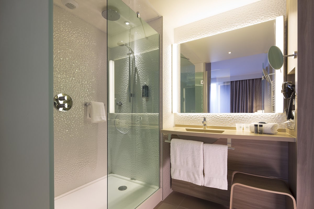 A modern bathroom with a glass-enclosed shower, a vanity with a mirror, and a towel rack.
