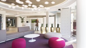 A modern lobby with a grey sofa, white and pink ottomans, and a round white table.