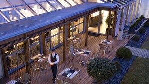 An outdoor dining area with tables and chairs, a waiter, and a glass-enclosed structure.