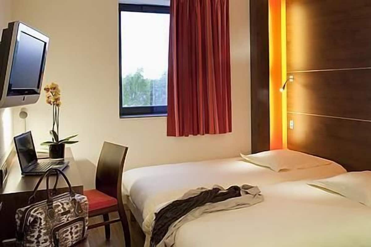 A hotel room with two beds, a desk with a laptop, a TV, and a window with curtains.
