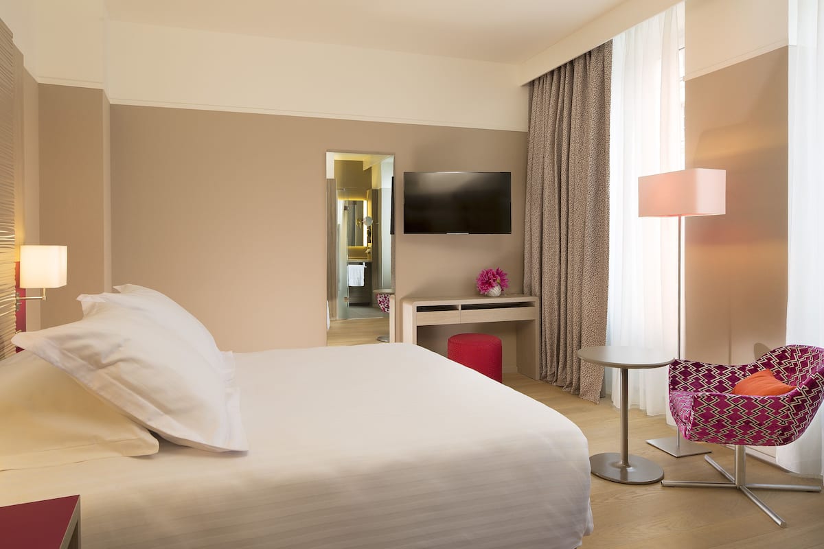 A hotel room with a bed, a desk, a chair, a TV, and a window with curtains.