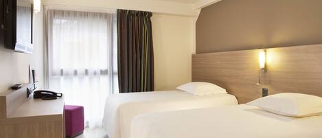 Habitación de hotel con dos camas, un escritorio con teléfono, televisor y ventana con cortinas.