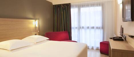 A hotel room with a large bed, a desk, a chair, and a TV.