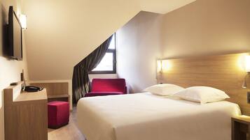 A hotel room with a bed, a desk, a chair, and a TV mounted on the wall.