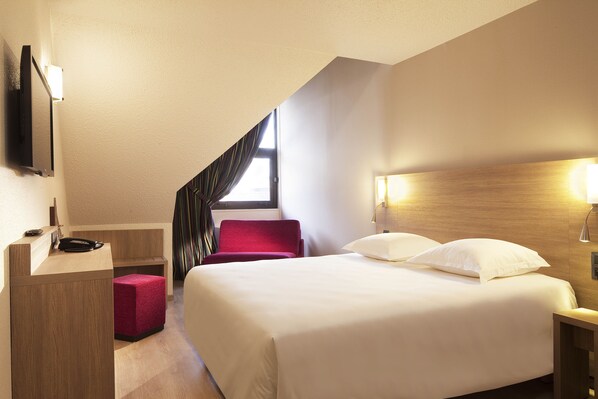 A hotel room with a bed, a desk, a chair, and a TV mounted on the wall.
