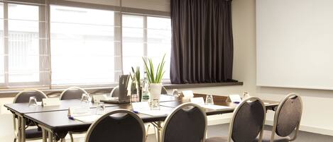 A conference room with a long table, chairs, a projector screen, and a large window with curtains.