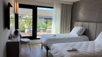 A hotel room with two beds, a desk, a chair, and a view of the outdoors.