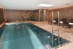 A modern indoor swimming pool with lounge chairs and a potted plant.