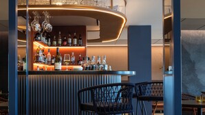 A bar area with a curved counter, wicker chairs, and a variety of bottles and glasses. - Hotel Oceania Saint Malo (Saint-Malo)