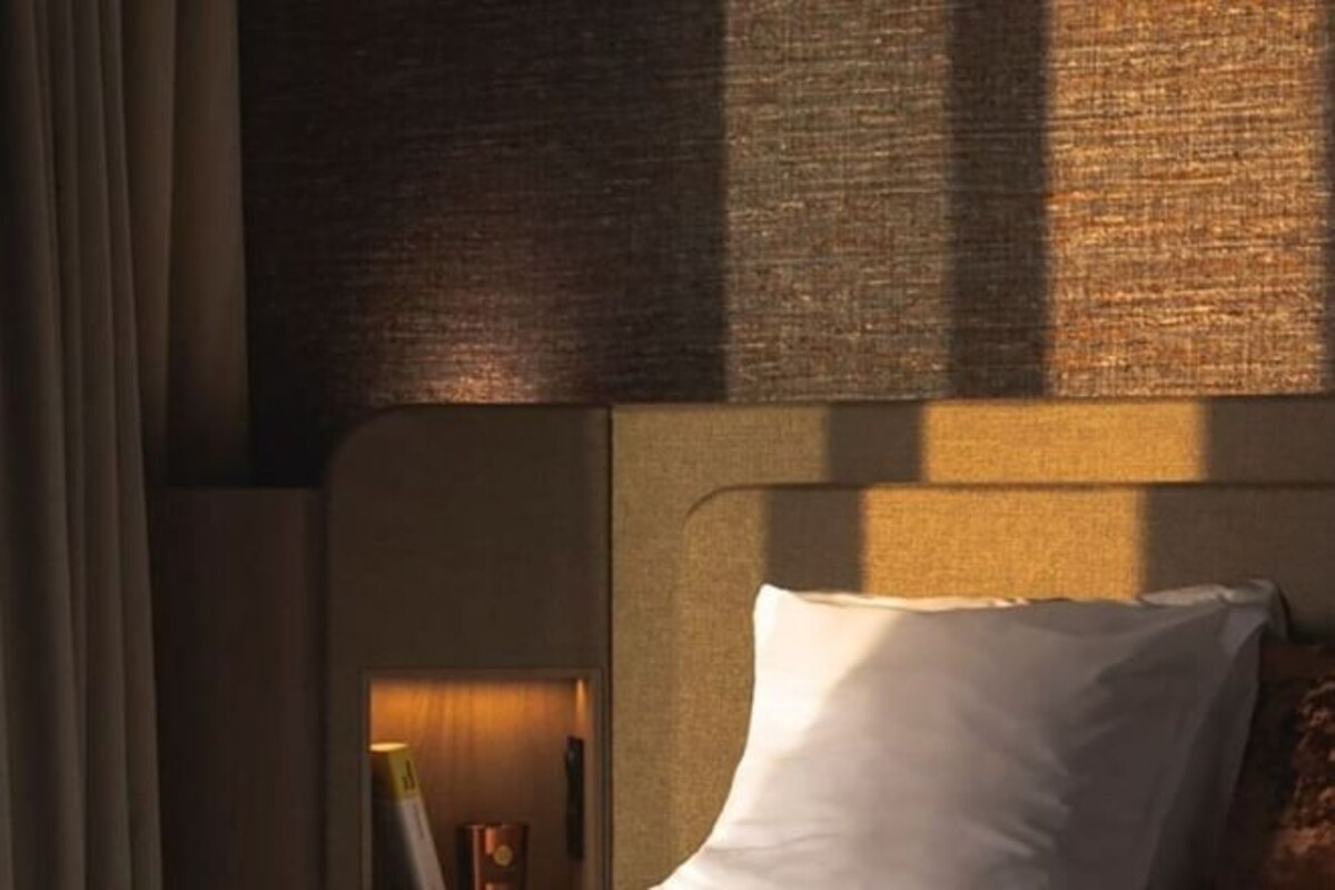 Quarto de hotel com cama, cabeceira e parede com textura.