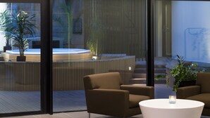 A modern indoor seating area with a round table and two brown armchairs, overlooking a hot tub and outdoor plants. - Hotel Oceania Saint Malo (Saint-Malo)