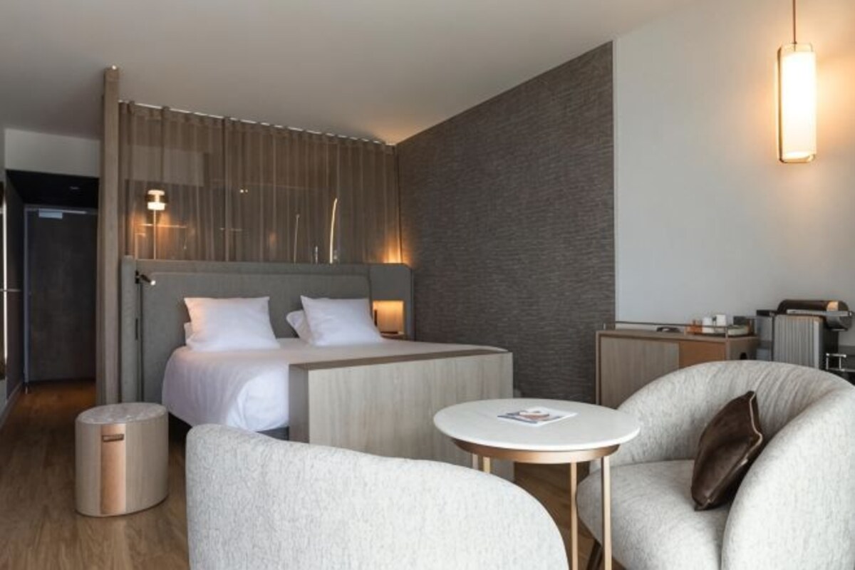 Quarto de hotel moderno com uma cama grande, um sofá, uma pequena mesa e uma escrivaninha.