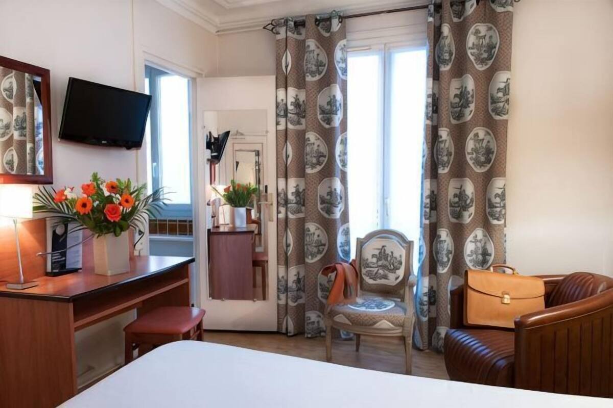 A hotel room with a bed, desk, chair, television, and curtains.