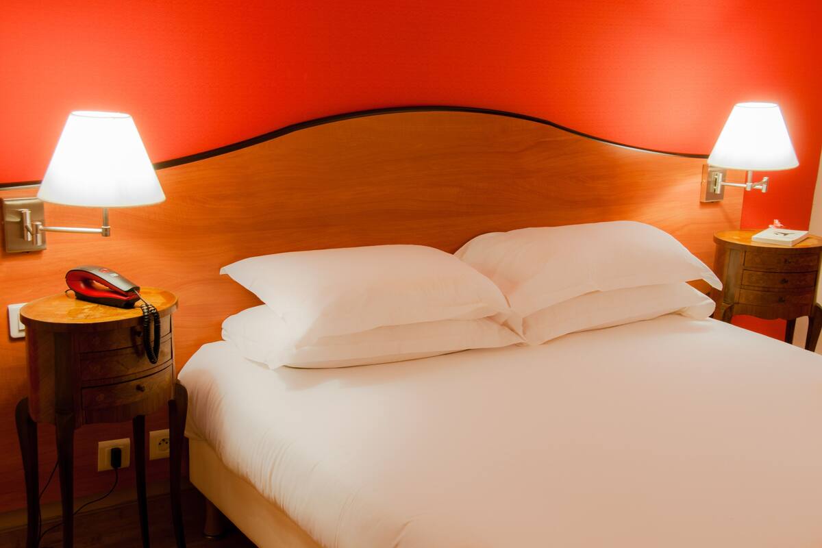 A hotel room with a wooden headboard, two bedside tables with lamps, a telephone, and a neatly made bed with white linens.