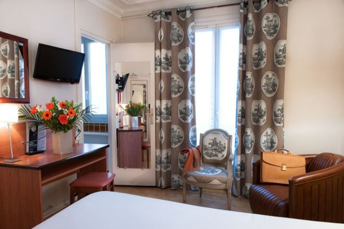 A hotel room with a bed, desk, chair, television, and curtains.