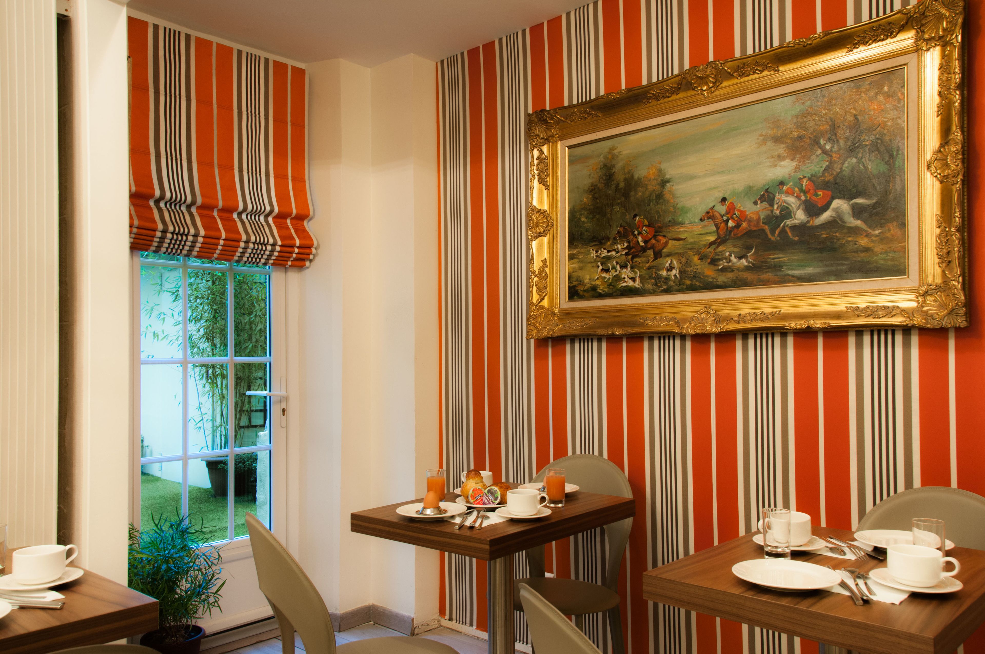 Een eetruimte met gestreepte behang, een lijstwerk schilderij en een tafel gedekt voor het ontbijt.