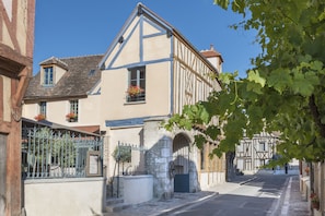 A traditional half-timbered building with a stone archway entrance, a small garden with flowers, and a clear blue sky.