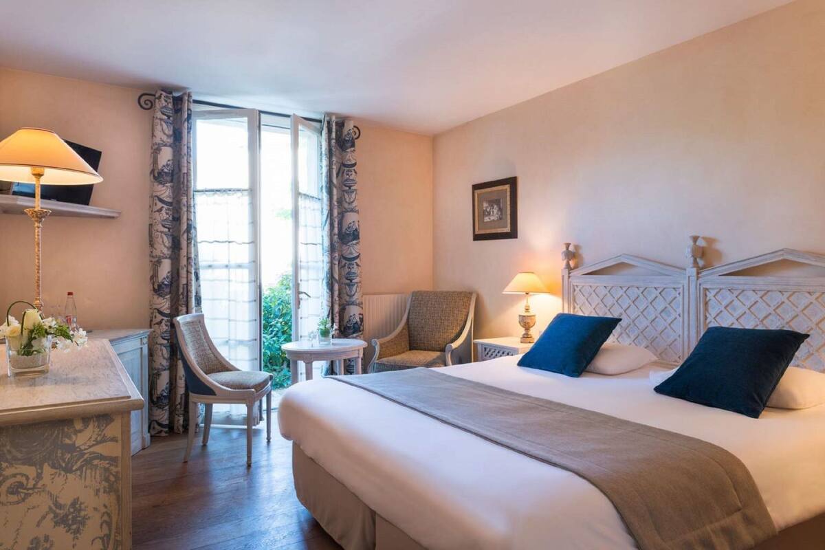 A hotel room with a large bed, two chairs, a desk, and a small table.