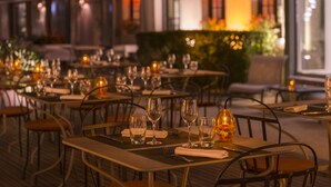 Un área de comedor al aire libre con mesas dispuestas para dos, cada una con una copa de vino y una vela.