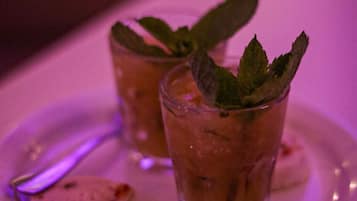 Two glasses of a beverage with mint leaves on a white plate, accompanied by a spoon.
