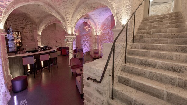 Interior de paredes de piedra con barra, asientos y una escalera.