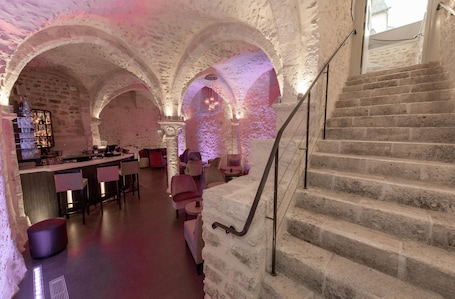 A stone-walled interior with a bar area, seating, and a staircase.