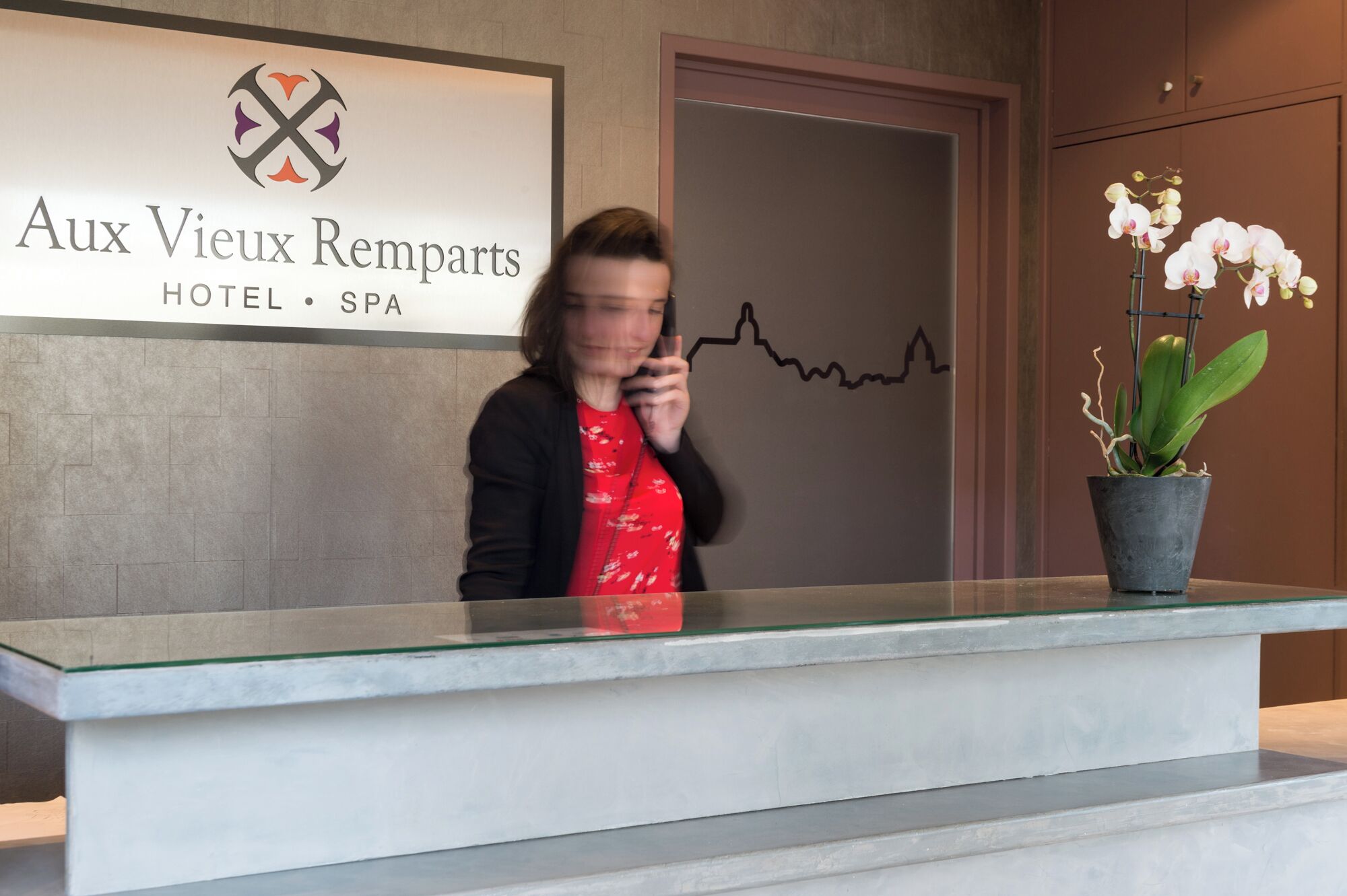 A hotel reception desk with a logo and name 'Aux Vieux Remparts HOTEL • SPA' above it.
